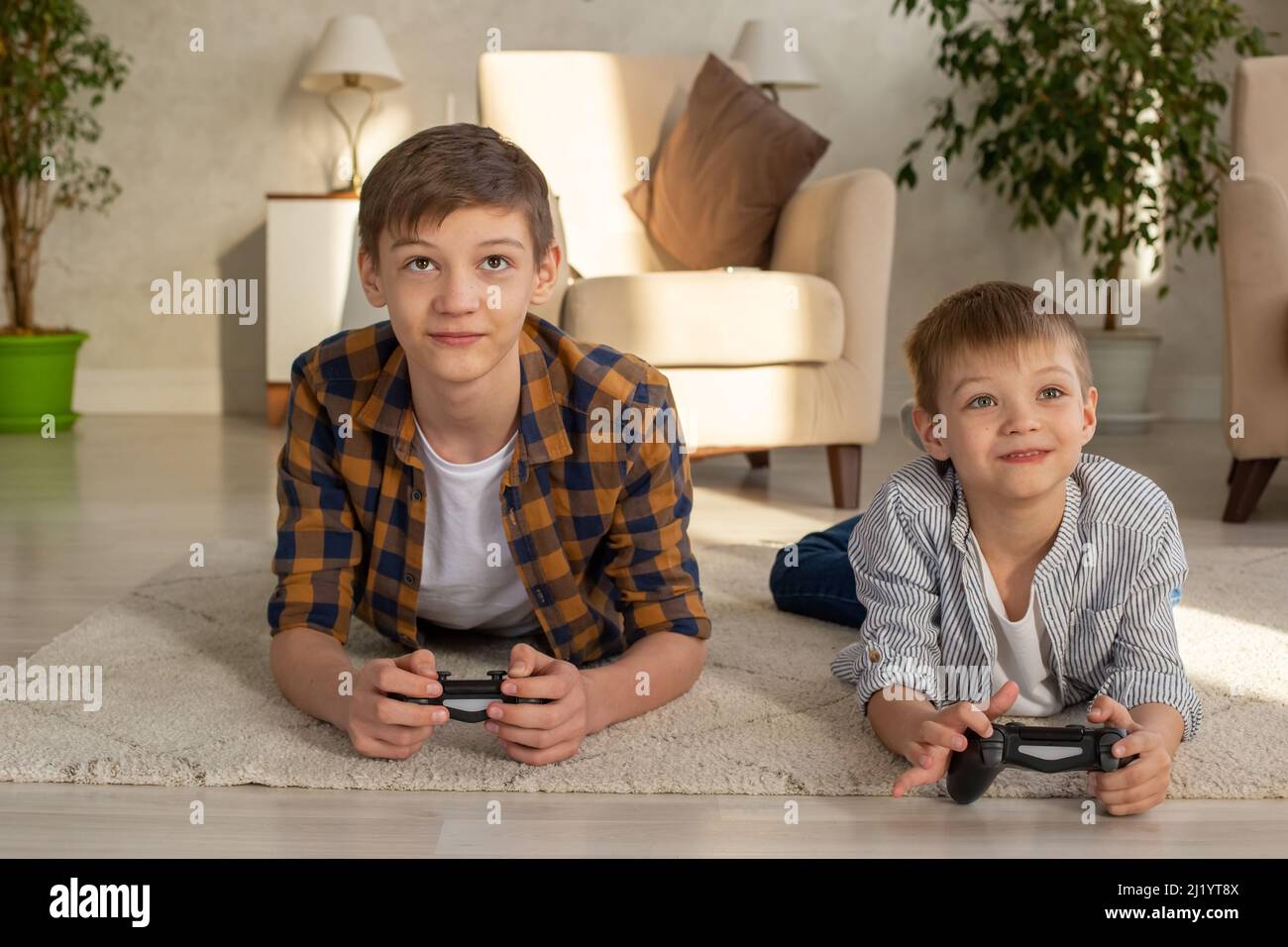 Ritratto di due ragazzi giacciono sul pavimento in una stanza che gioca video giochi con joystick Foto Stock