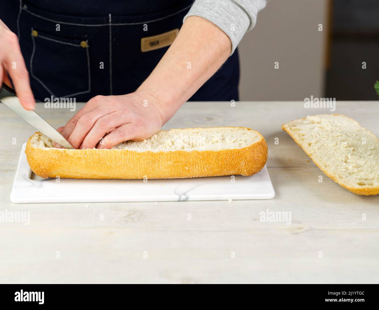 il cuoco taglia il pane fresco di ciabatta. Estrae la polpa dall'interno. Consente di preparare il pane in modo semplice. Processo di preparazione dei sandwich molto ampio. Foto Stock