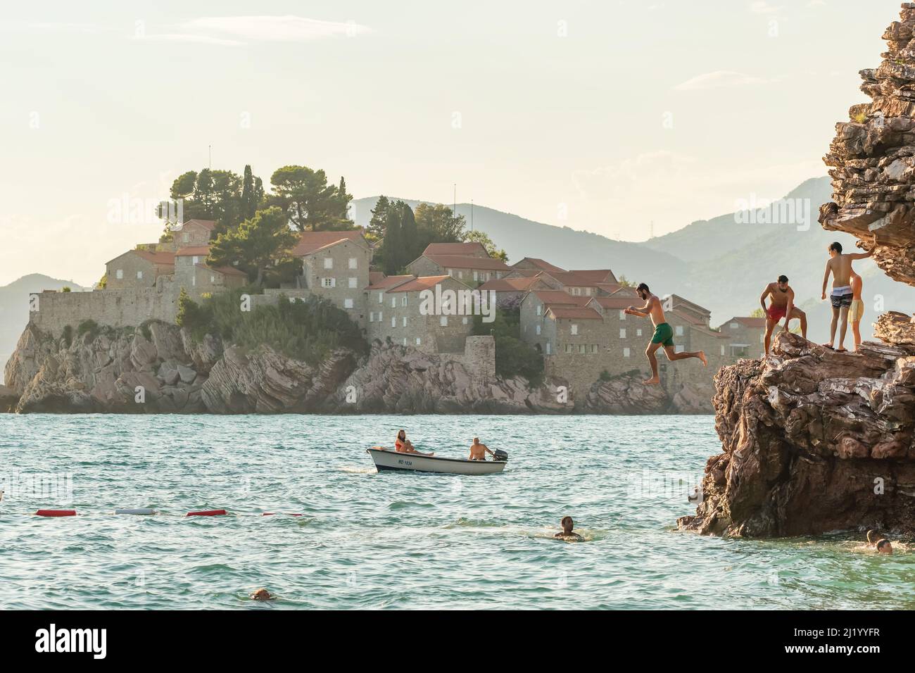 Scogliera tuffarsi nel mare con la famosa isola Sveti Stefan sullo sfondo in Montenegro. Foto Stock