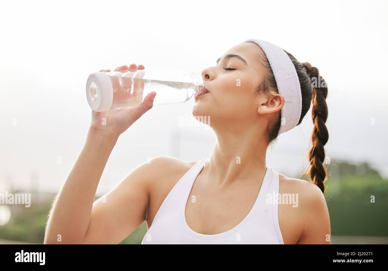 Non riesco a fare abbastanza. Scatto di una bella giovane donna che beve una bottiglia d'acqua mentre fuori giocando a tennis. Foto Stock