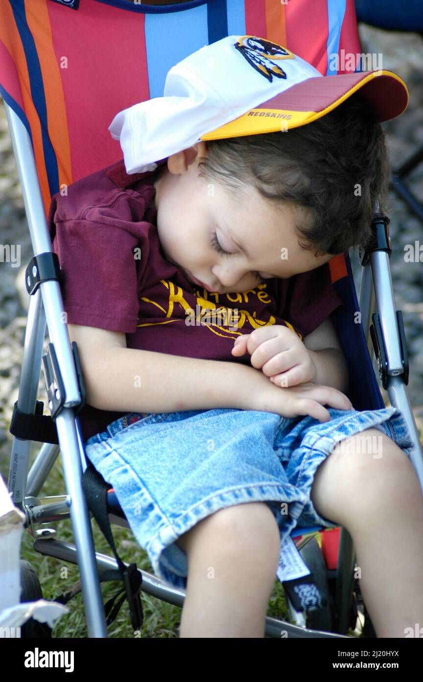 Bambino ragazzo, toddler, che dorme in stroller al gioco della sfera con i genitori con il logo Redskins sul cappello con il suo volto Foto Stock