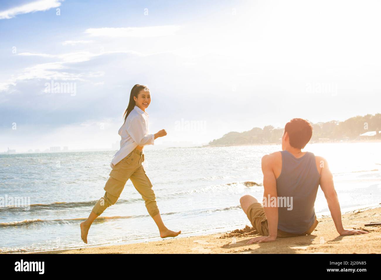 Un giovane seduto sulla spiaggia che guarda una giovane donna - foto di scorta Foto Stock