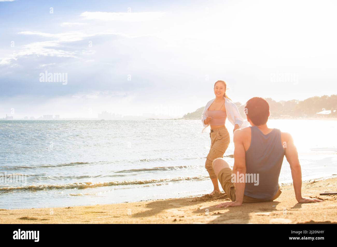 Un giovane seduto sulla spiaggia che guarda una giovane donna - foto di scorta Foto Stock