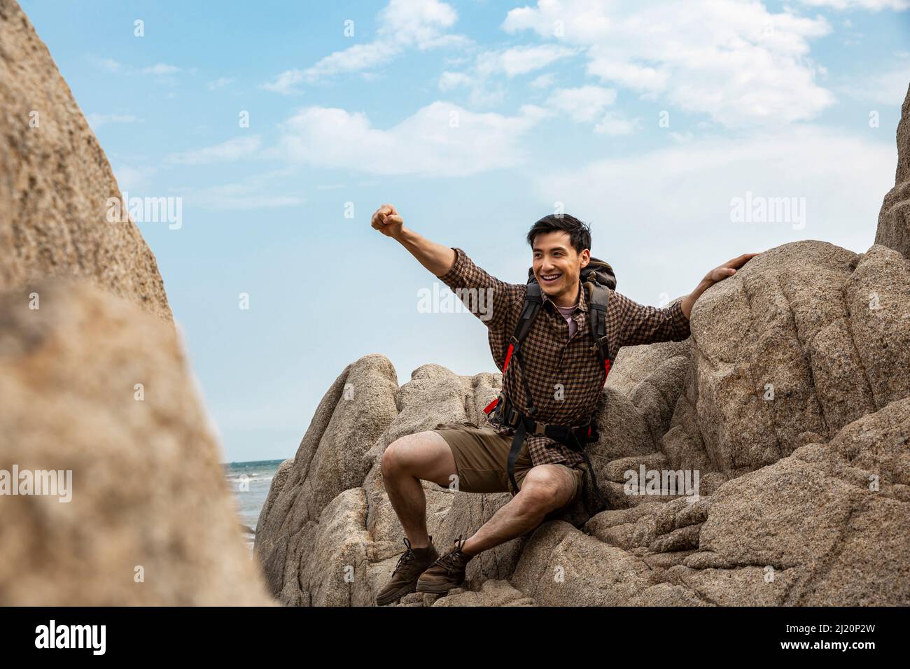 Zaino in spalla giovane con braccia distese sulle rocce della spiaggia - foto di scorta Foto Stock