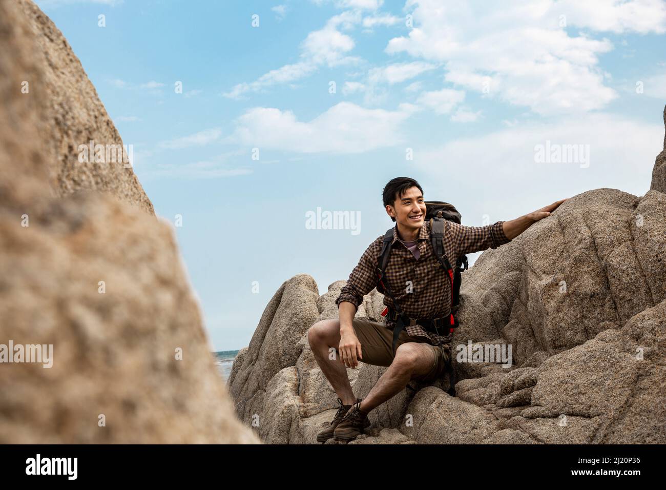 Giovane outdoorsman seduto su una roccia da spiaggia guardando il paesaggio - foto di scorta Foto Stock