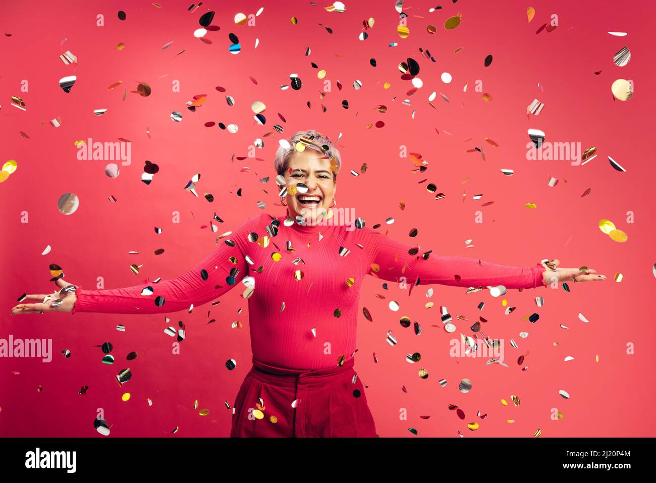 Confetti! Spensierate la giovane donna che si eccita mentre si alza sotto i confetti cadenti in uno studio. Giovane donna vibrante che si diverte e festeggia la vita Foto Stock