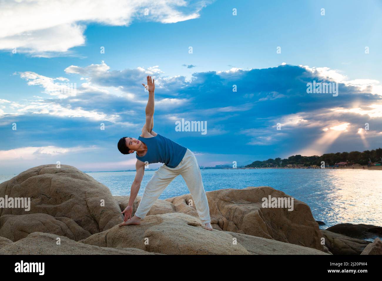 Giovane uomo muscoloso che fa yoga su una roccia da spiaggia - foto di scorta Foto Stock