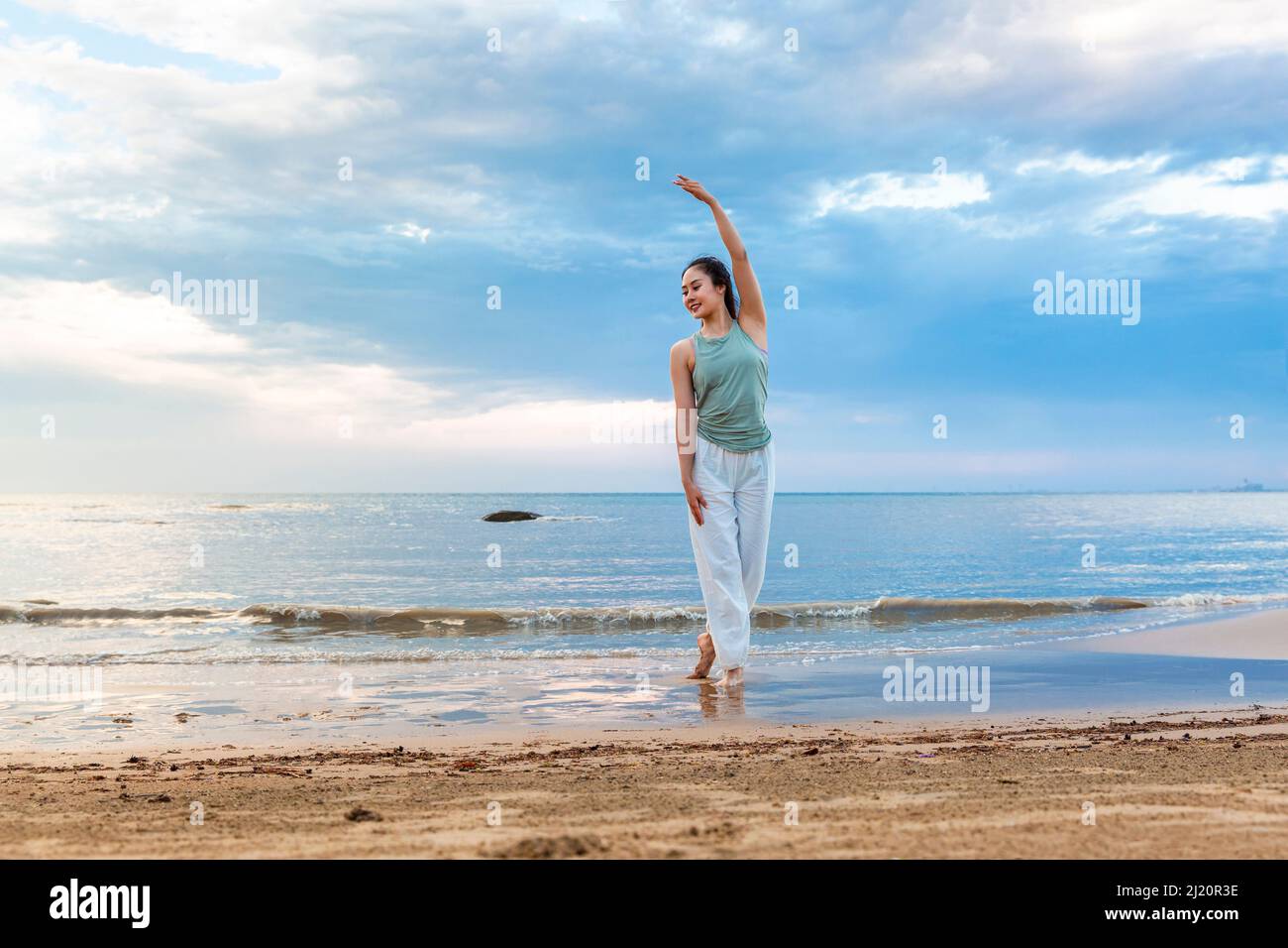 Giovane donna che pratica yoga da sola su una spiaggia estiva - foto di scorta Foto Stock