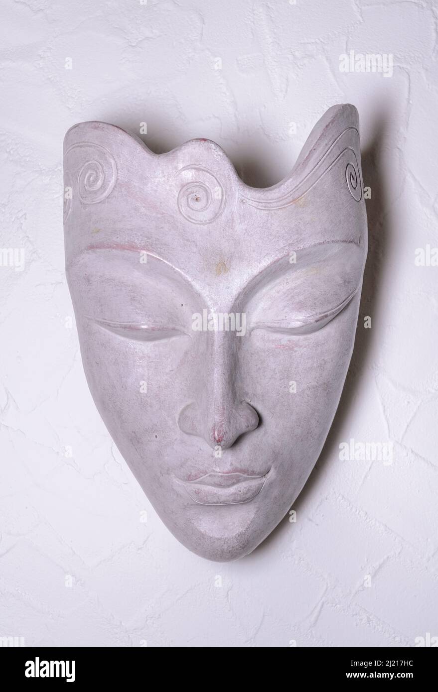 Maschera decorativa asiatica o orientale fatta di pietra grigia su una parete bianca, vista frontale Foto Stock