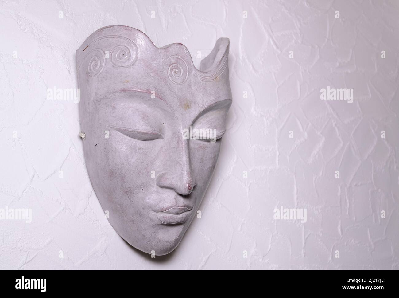 Maschera decorativa asiatica o orientale fatta di pietra grigia su una parete bianca, vista frontale Foto Stock