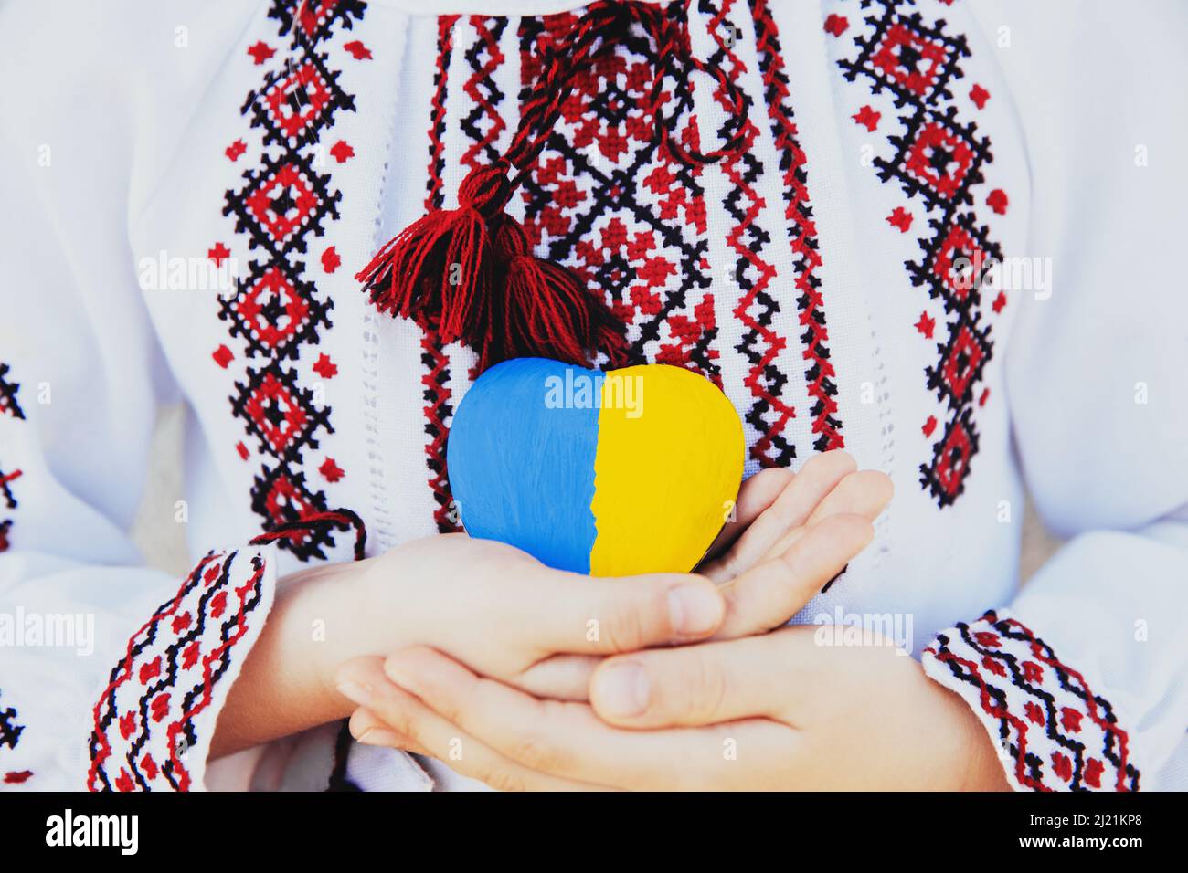 Piccola bambina in ricamo tradizionale nazionale o camicia ricamata mantiene la forma del cuore di pietra con la bandiera nazionale di Ukrane. Ami il paese e la gente autoctona. Prega per pezzo Ucraina. Foto di alta qualità Foto Stock