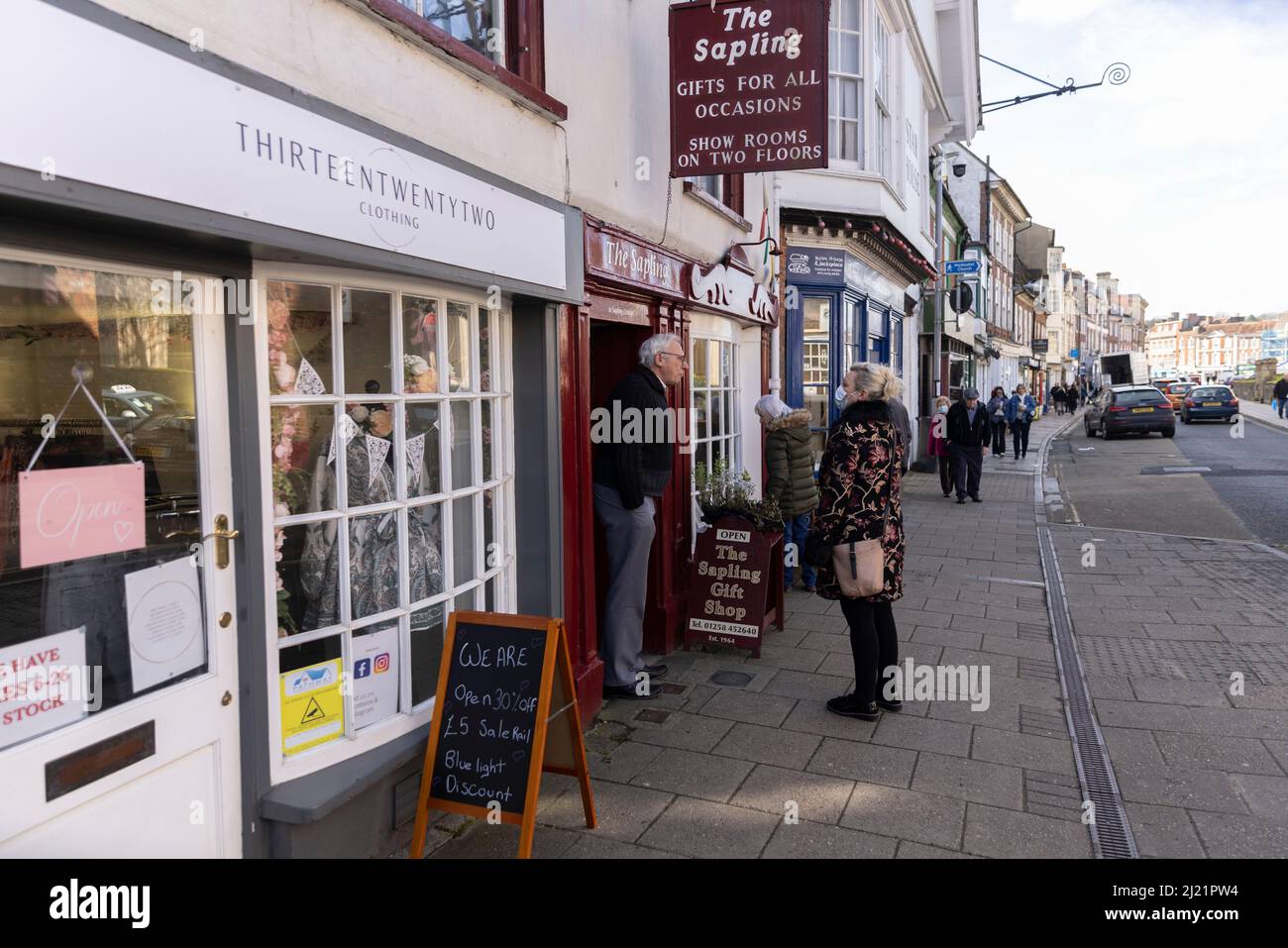 Un negoziante che ha una chiacchierata con una signora locale sulla strada principale, Blandford Forum, Dorset, Inghilterra, Regno Unito Foto Stock