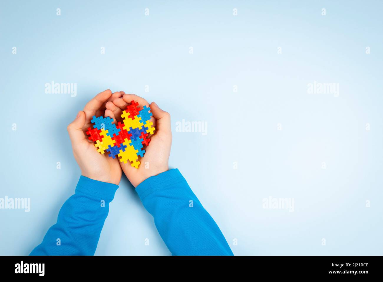 Bambino mano che tiene colorato puzzle cuore su sfondo azzurro chiaro. Concetto di giornata di consapevolezza autismo mondiale Foto Stock