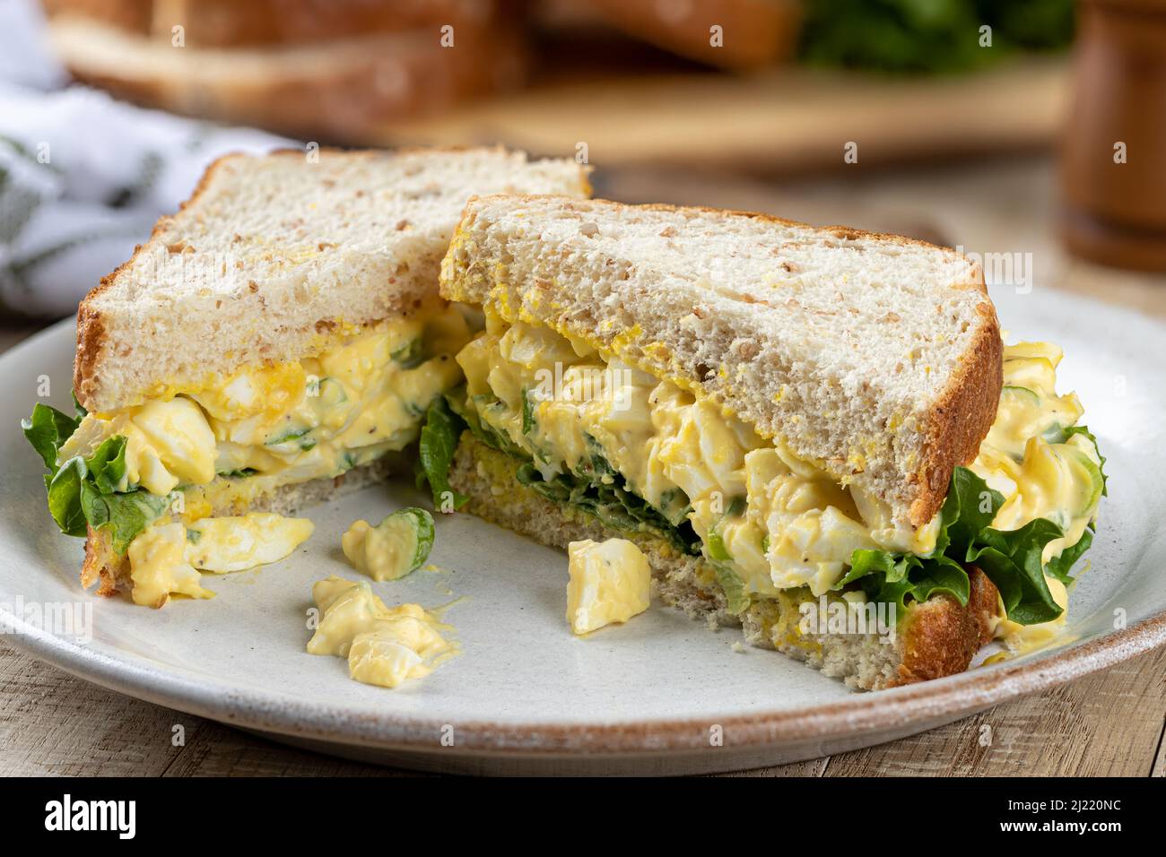 Primo piano di un sandwich di insalata di uova con lattuga su pane intero di grano tagliato a metà su un piatto Foto Stock