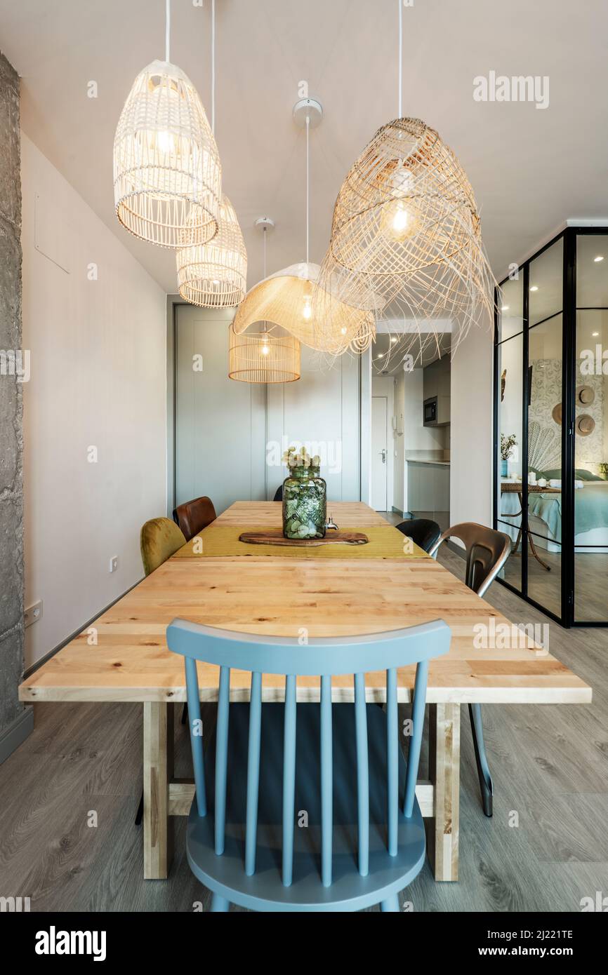 Soggiorno con tavolo da pranzo in legno, sedie in legno e metallo e lampade in vimini Foto Stock