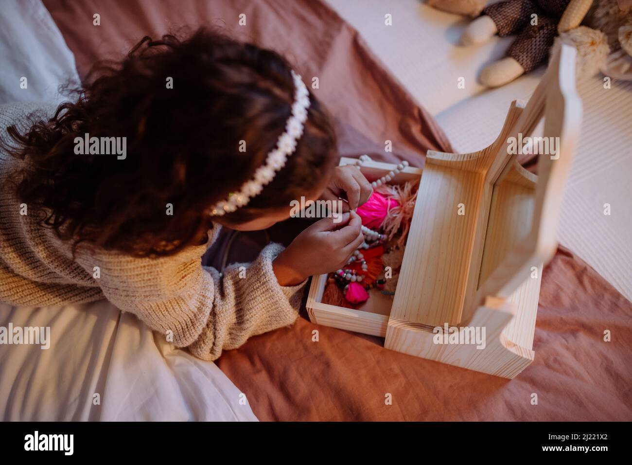 Piccola ragazza multirazziale che si trova a letto e guardando le sue posate a casa, vista dall'alto. Foto Stock