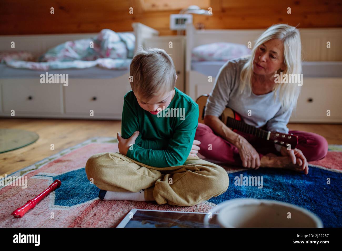 Ragazzo con sindrome di Down seduto a terra e giocando con la nonna a casa Foto Stock