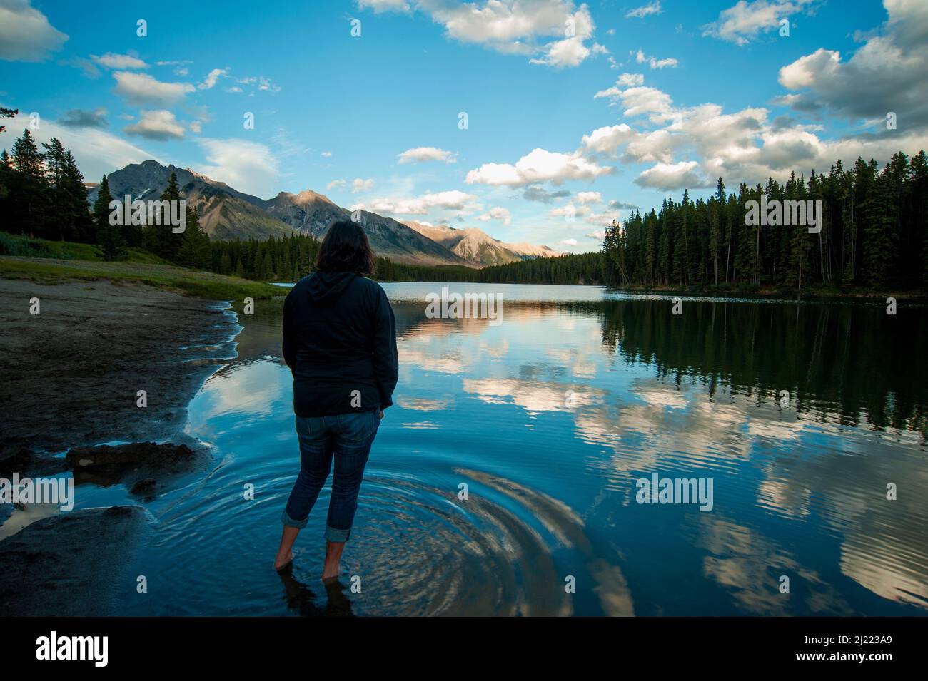 Donna in piedi in acque poco profonde del lago Johnson nel Parco Nazionale di Banff guardando le montagne e la scena rurale. Foto Stock