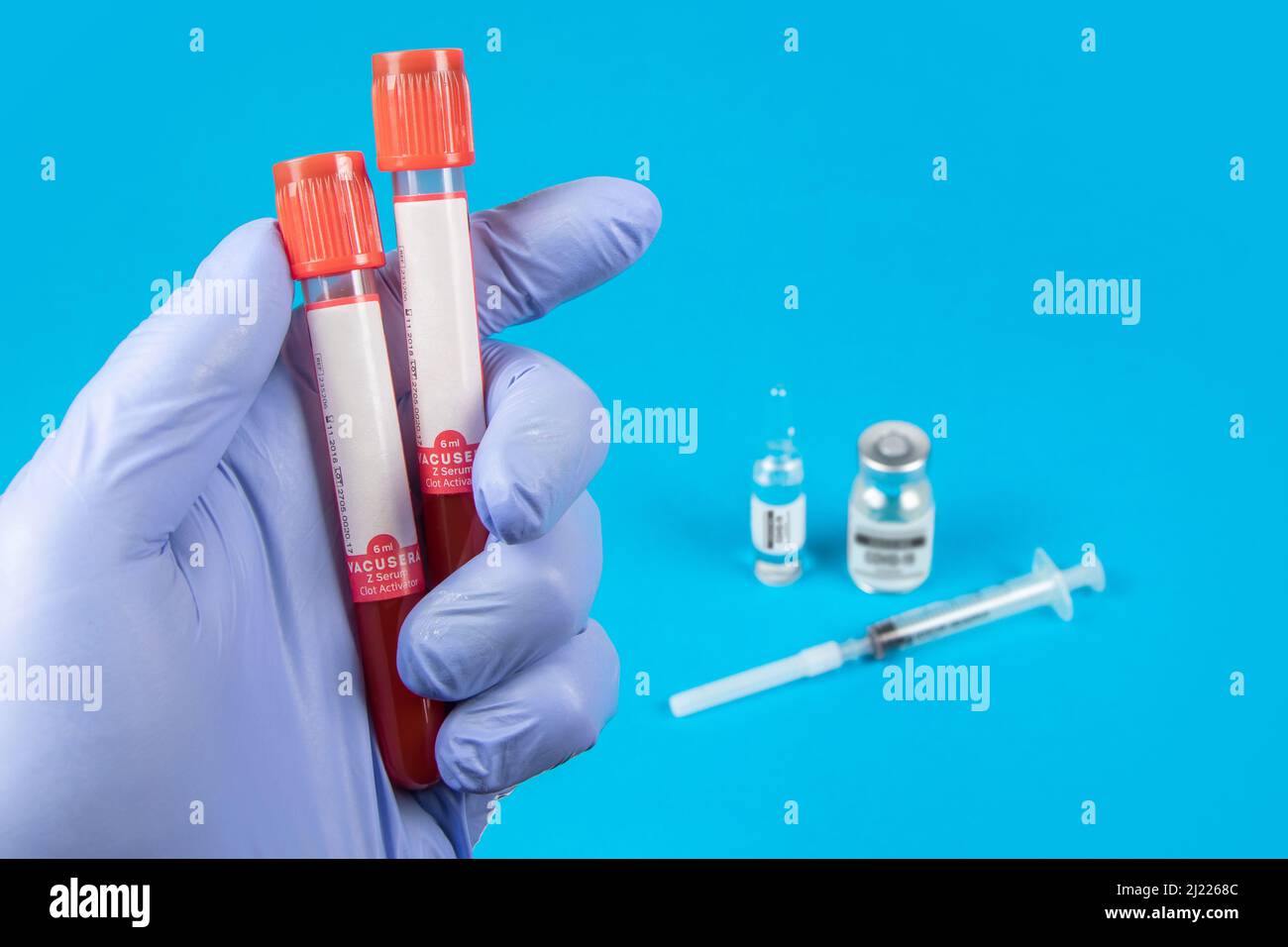 Mano di un medico che tiene un flacone di campione di sangue. Sfondo blu Foto Stock