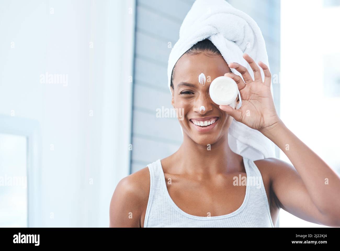 Credo nel prendersi cura della mia pelle. Scatto di una bella giovane donna che applica moisturizer al suo viso. Foto Stock