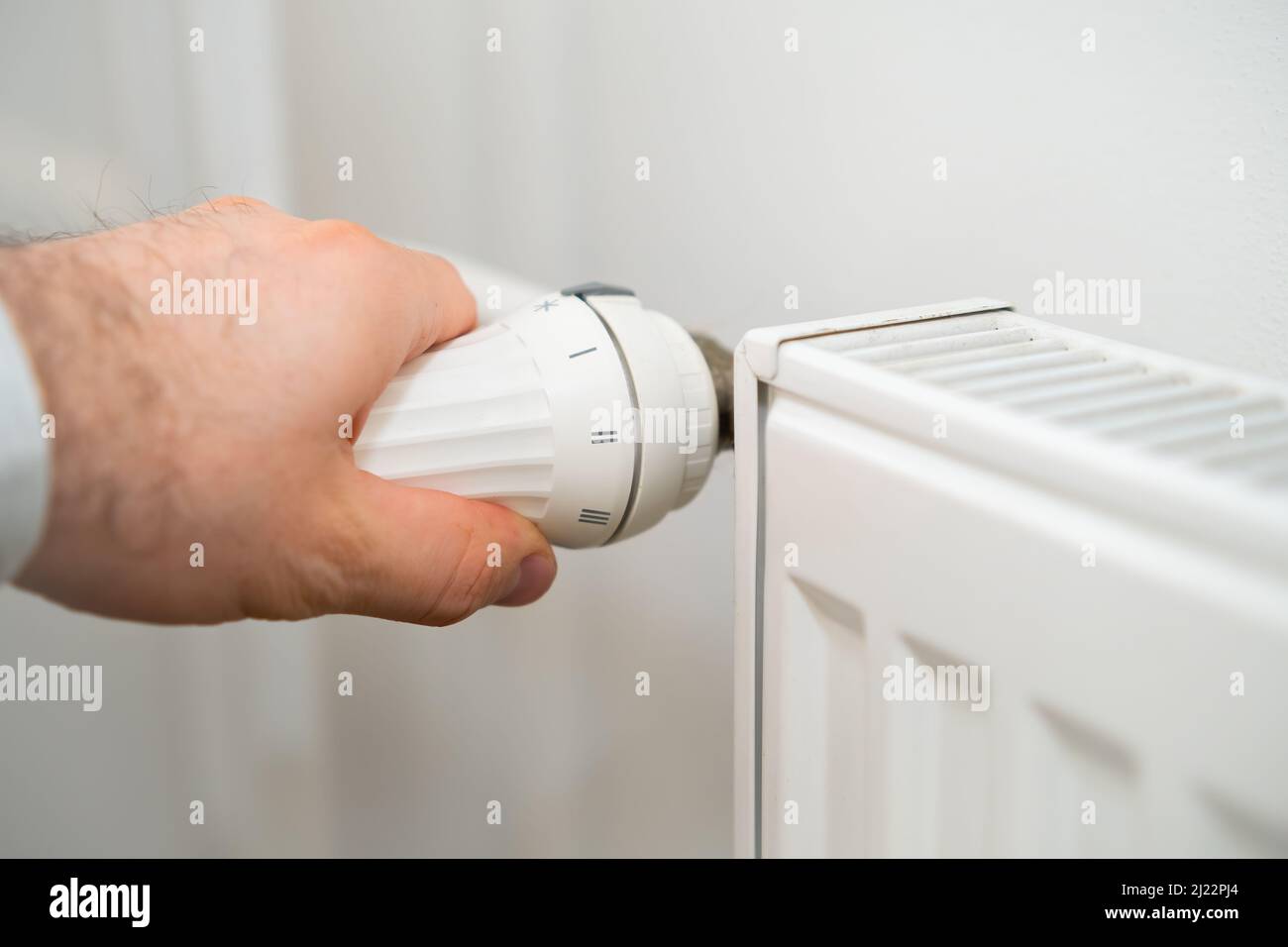 Man Hand regola la manopola di regolazione della temperatura del radiatore di riscaldamento per ridurre i costi di riscaldamento. Foto Stock