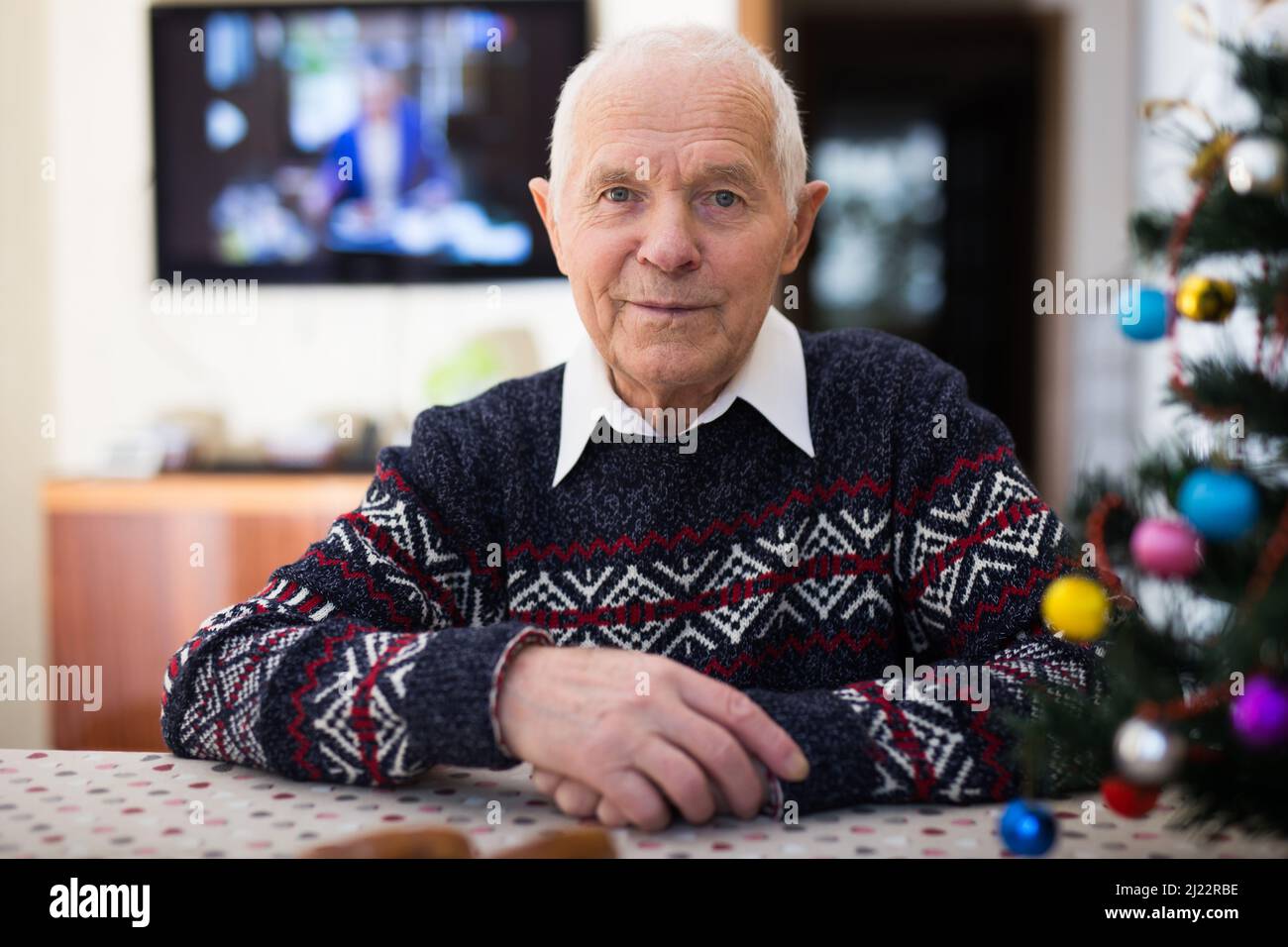 Uomo anziano positivo seduto da solo a casa con albero di Natale Foto Stock