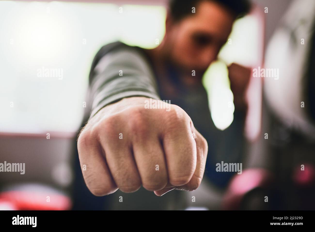 È il momento di mettere questi ragazzi al lavoro. Primo piano di un giovane pugile maschio concentrato che lancia punzoni alla macchina fotografica all'interno di un anello in palestra durante il giorno. Foto Stock