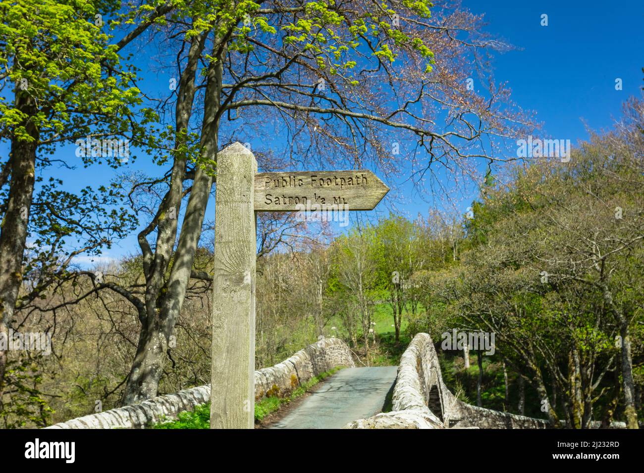 Sentiero pubblico segno a Satron, un borgo rurale di Swaledale, con 16th secolo Ivelet Bridge sullo sfondo. Primavera nello Yorkshire Dales wi Foto Stock