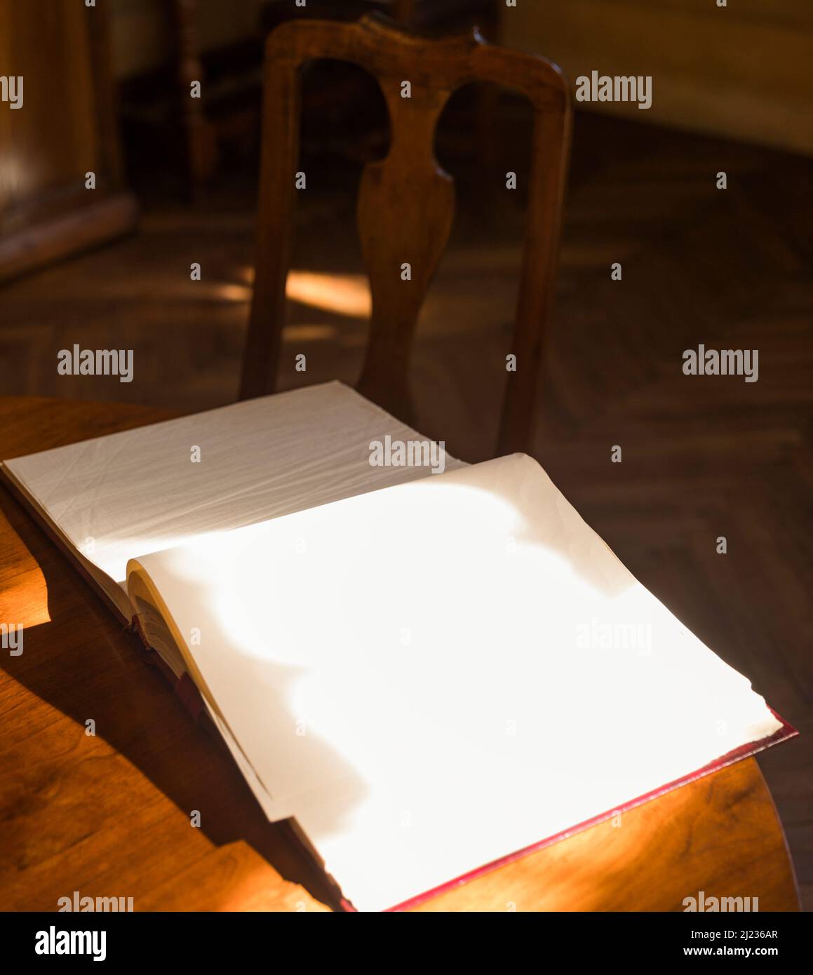 apri un libro su una scrivania in legno con luce solare che illumina una pagina vuota Foto Stock