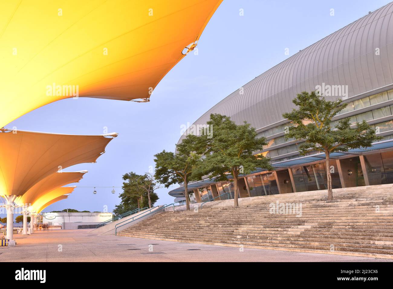 Altice Arena edificio moderno esterno e passerella con strutture a membrana tensile illuminate al crepuscolo, Parque das Nacoes distretto di Lisbona Portogallo. Foto Stock
