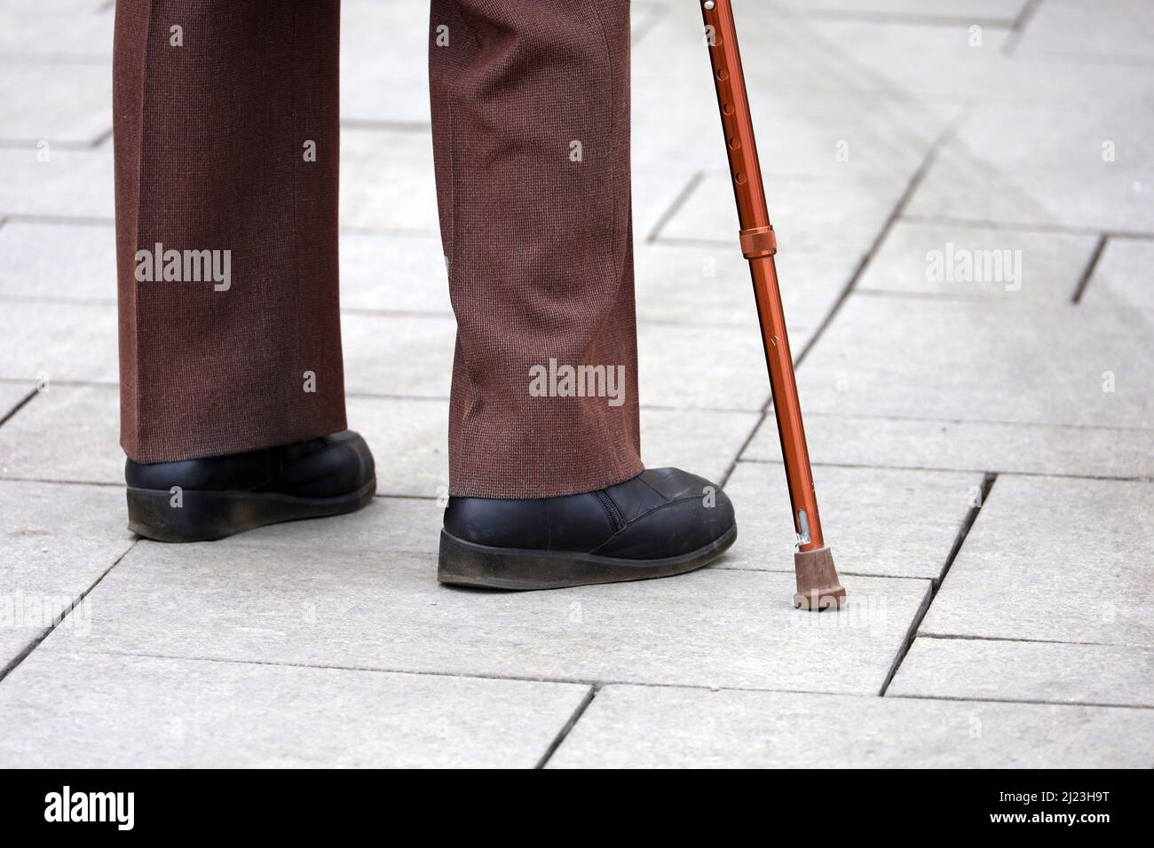 Uomo con bastone da passeggio su una strada, gambe maschili in pantaloni sul marciapiede. Concetto di invalidità, persona che limping Foto Stock