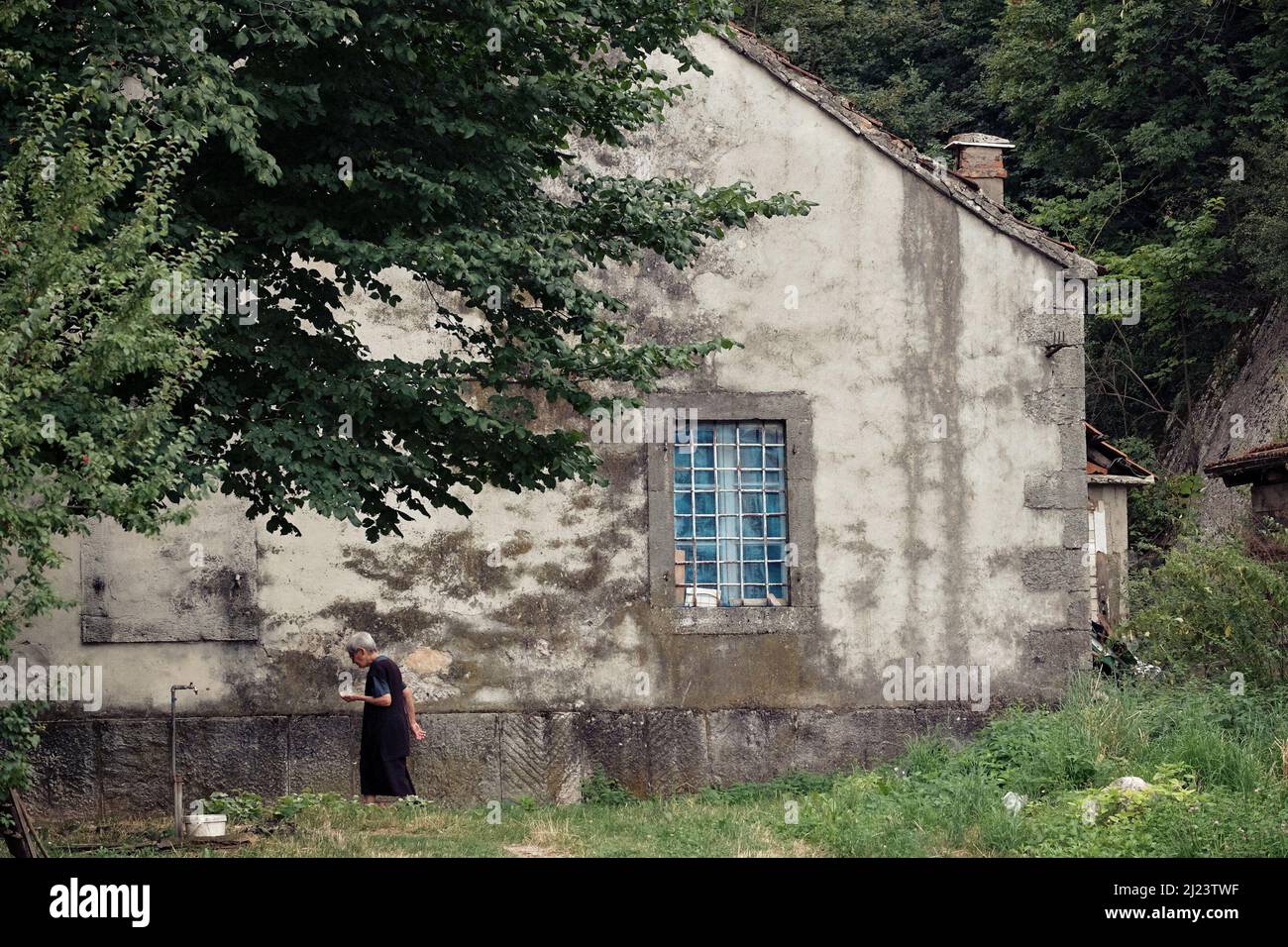 NIKSIC, MONTENEGRO - 25 LUGLIO 2016: Donne anziane di profilo vestite di nero passa lungo il lato di una grande casa di campagna Foto Stock