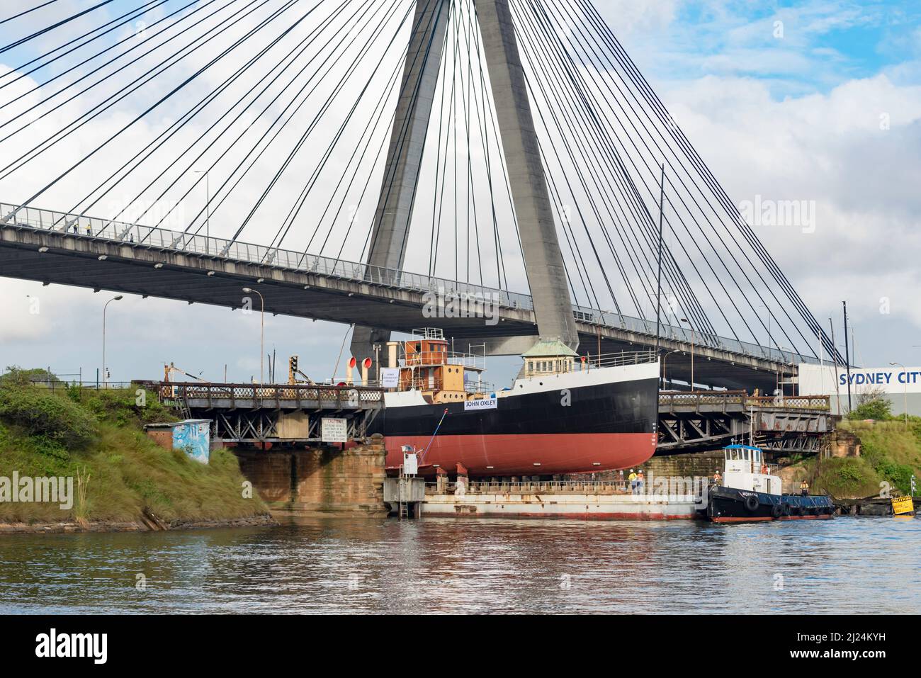 30 marzo 2022, Glebe Island Bridge, Sydney, Australia: La nave a vapore costiera del 1927, John Oxley che ha subito anni di restauro e conservazione è qui raffigurato sulla sua strada per essere finalmente refloated dopo 21 anni montato su un pontone presso i laboratori della Sydney Heritage Fleet a Roselle Bay. Dopo aver rimosso facilmente l'enorme ponte in cemento ANZAC, il pontone si adatta solo attraverso l'apertura del vecchio ponte dell'isola di Glebe sulla strada per un molo asciutto a Garden Island, più in basso nel porto di Sydney, dove sarà accuratamente rifocillato e testato. Foto Stock