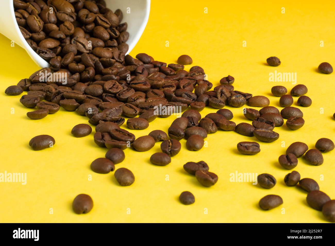 Tazza da caffè di carta bianca da asporto su sfondo giallo con i chicchi tostati che si versano fuori Foto Stock