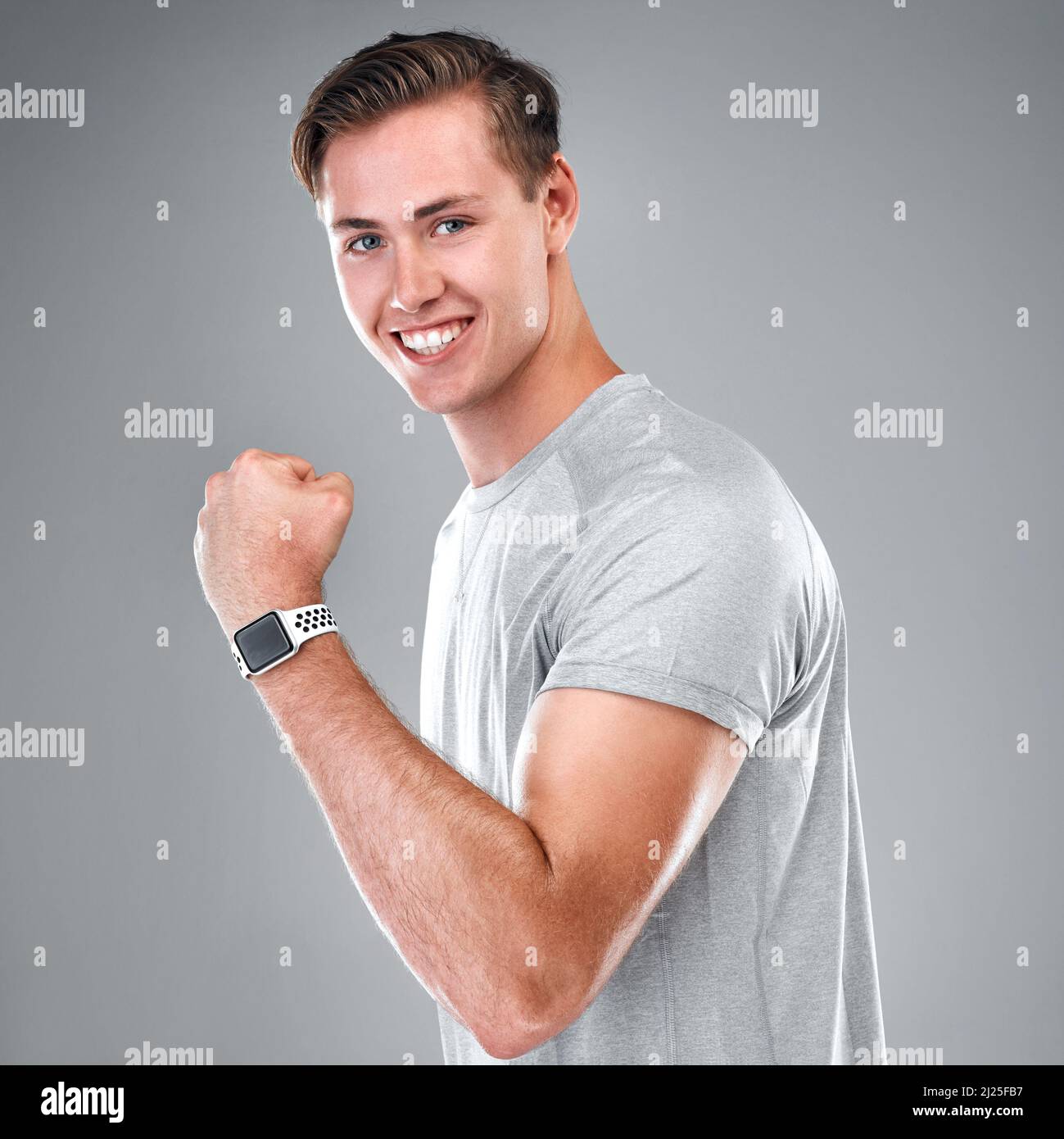 Flessibile. Ritratto corto di un bel giovane uomo in piedi da solo su uno sfondo grigio studio e flettendo il suo bicep. Foto Stock