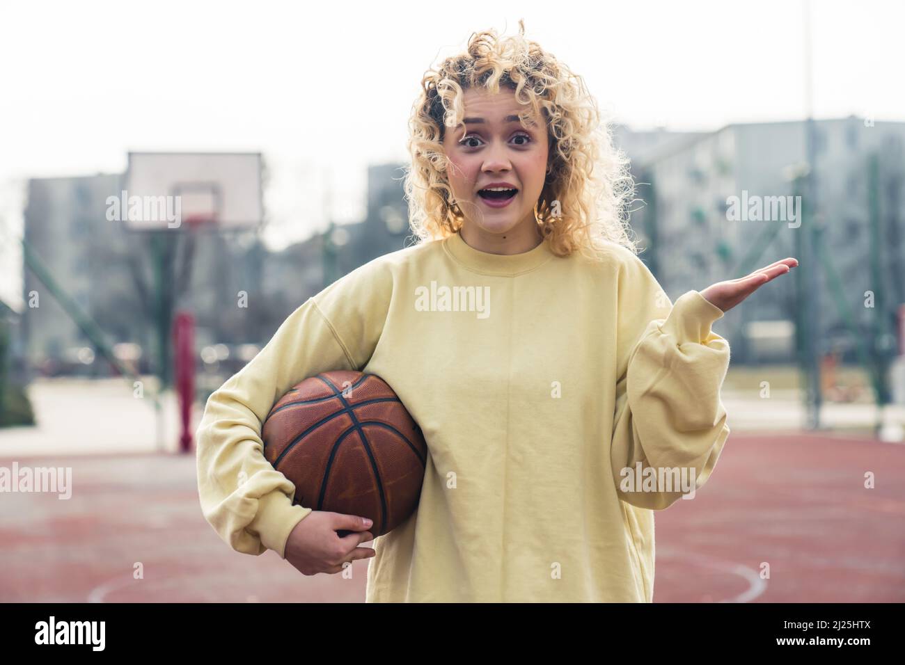 La giovane donna eccitata bionda millennial tiene una palla di basket e la tiene un'altra mano aperta ritratto copia spazio . Foto di alta qualità Foto Stock