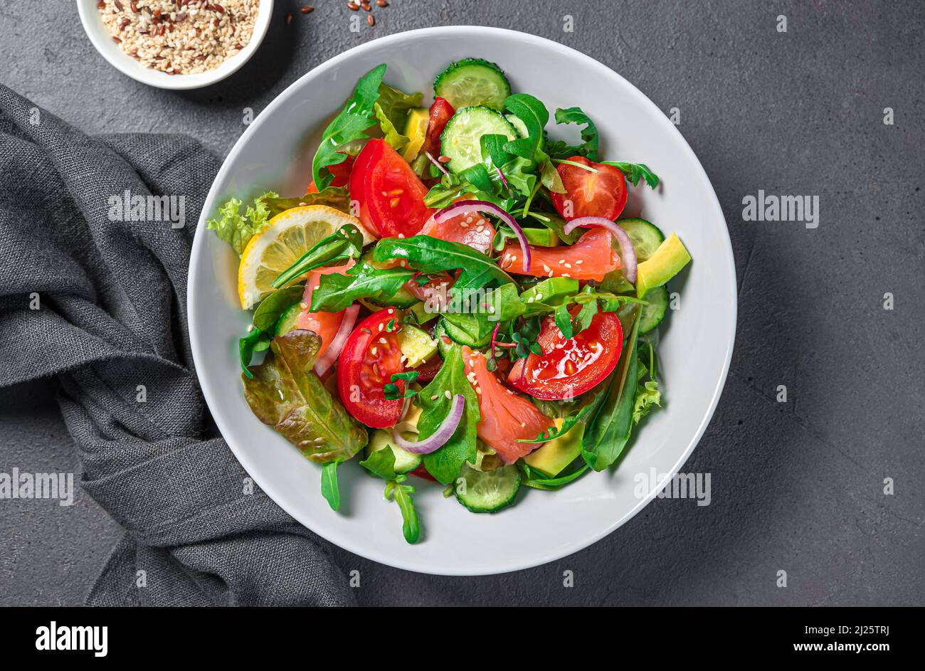 Insalata fresca con salmone, avocado, cetrioli e pomodori su sfondo scuro. Foto Stock
