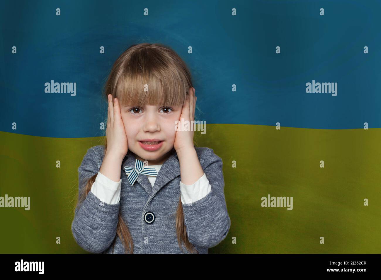 La bambina spaventata copre le orecchie con le mani in modo da non sentire nulla contro la bandiera Ucraina sfondo. Fermare la guerra in Ucraina Foto Stock