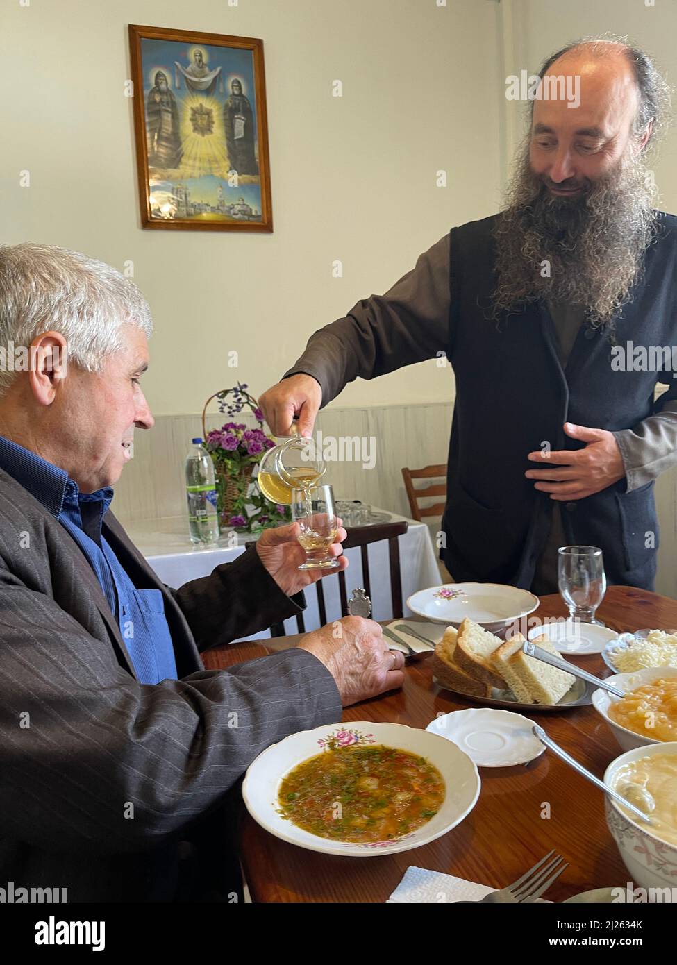 I fedeli hanno offerto il pranzo nel monastero ortodosso di Rudi, in Moldavia. Abbot servire il vino Foto Stock