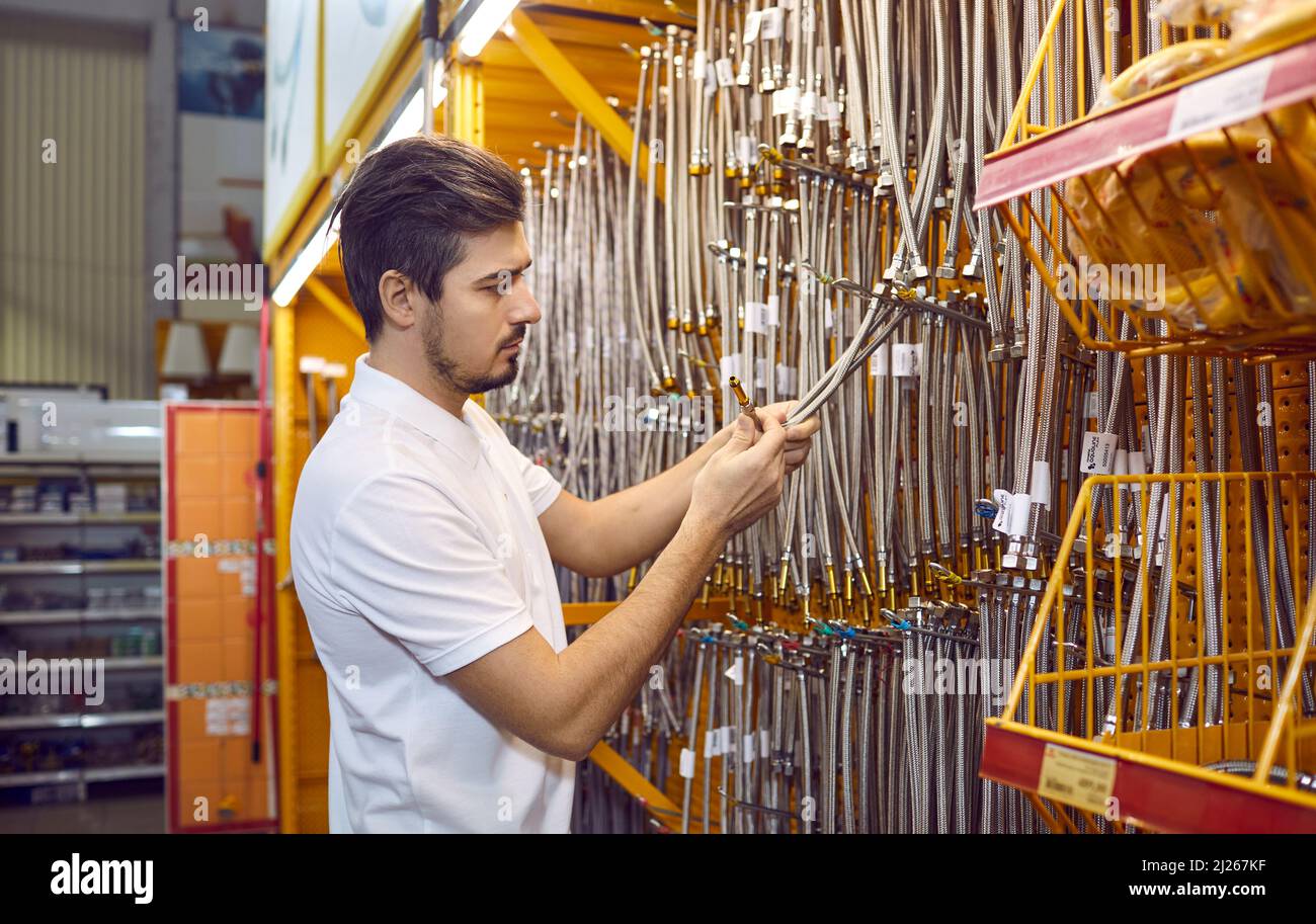 Il cliente maschio presso lo scaffale del negozio di ferramenta sceglie tubi flessibili in acciaio inossidabile. Foto Stock