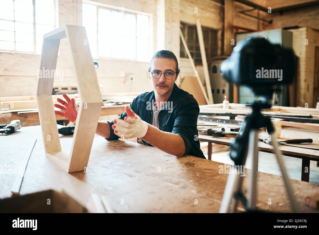 I miei video fai da te sono sempre online. Scatto di giovane carpentiere che registra un tutorial di lui facendo un capolavoro di legno su una videocamera all'interno del suo Foto Stock