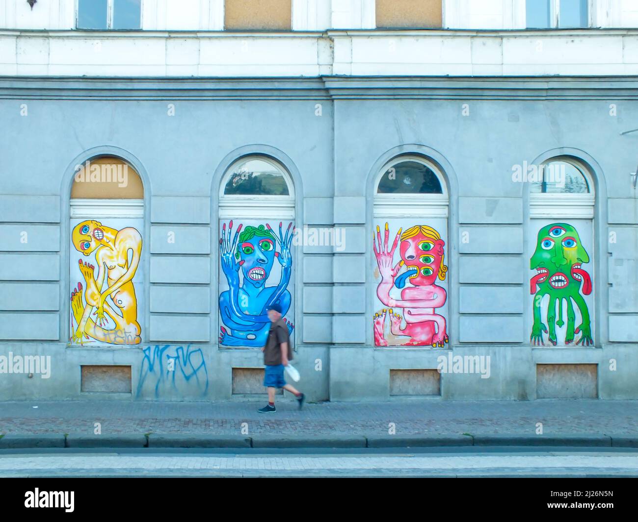Praga, Repubblica Ceca-13 giugno 2015: Un uomo cammina lungo un muro con graffiti colorati nella strada, Una facciata edificio con graffiti su finestre ad arco Foto Stock