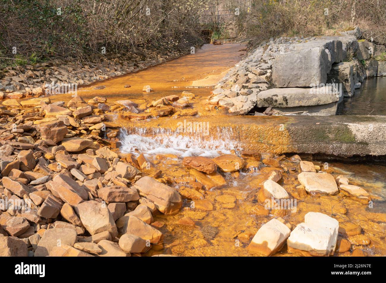 Colorazione arancione ossido di ferro in corrente che entra nel fiume Neath ad Abergarwed. La fonte è lo scarico di acqua da una miniera di carbone abbandonata. Foto Stock