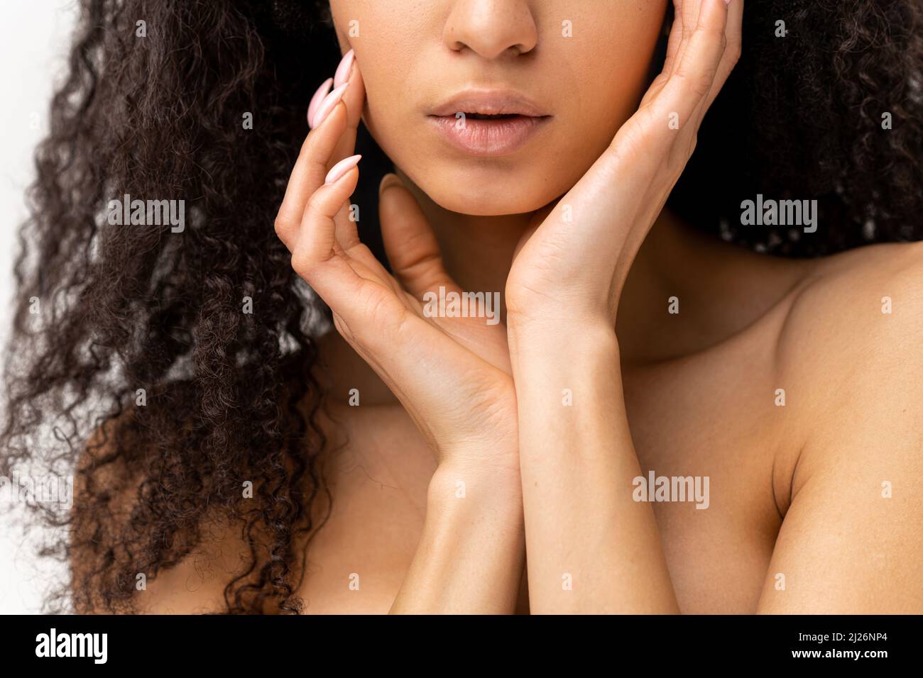 Signora affascinante si erge isolato su sfondo bianco. Vista ritagliata a sensuale nuda multirazziale bella donna sta toccando delicatamente il suo corpo di fronte alla fotocamera. Concetto di cura del corpo e del viso Foto Stock