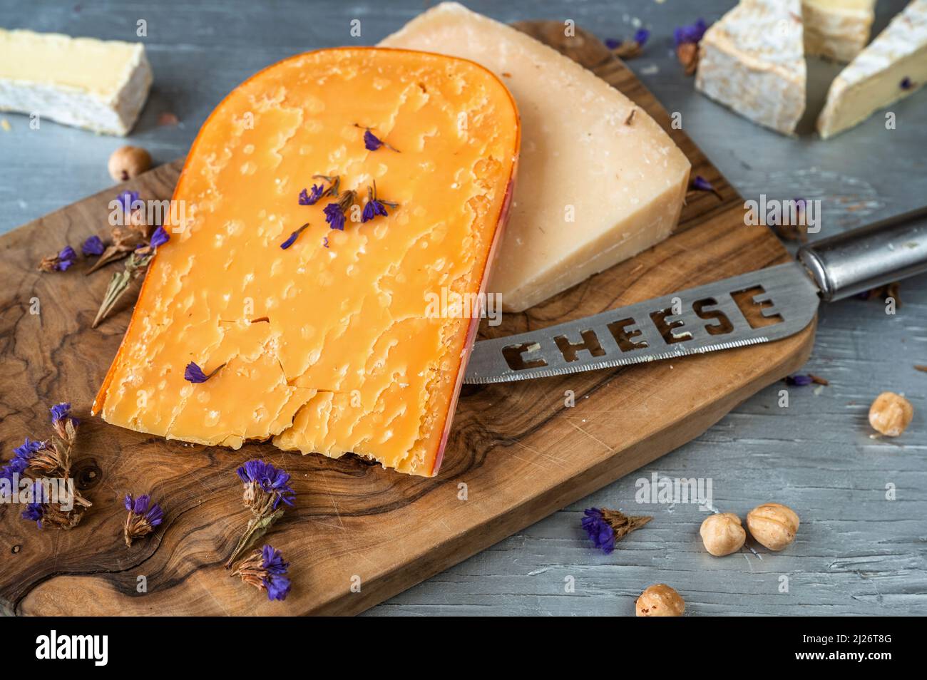 Sfondo di formaggio. Pezzo di formaggio a fette, coltello con iscrizione 'formaggio', dado su tagliere di legno su tavola. Foto Stock