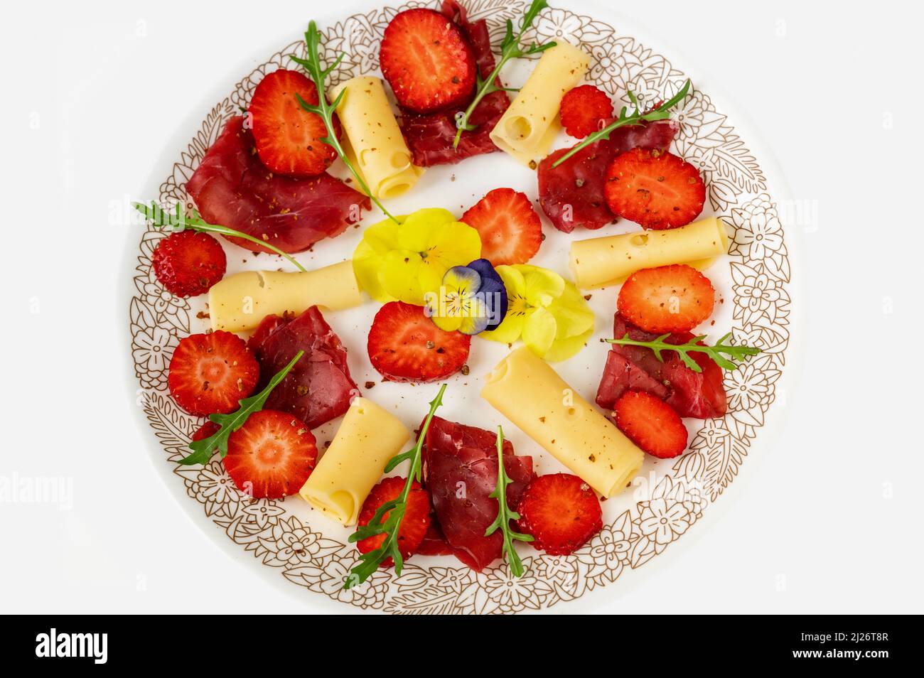 Antipasto leggero (o portata principale) con fragola, formaggio e carpaccio, testa di fiori alla pancia commestibile e foglia di rucola sul piatto, isolato su sfondo bianco Foto Stock