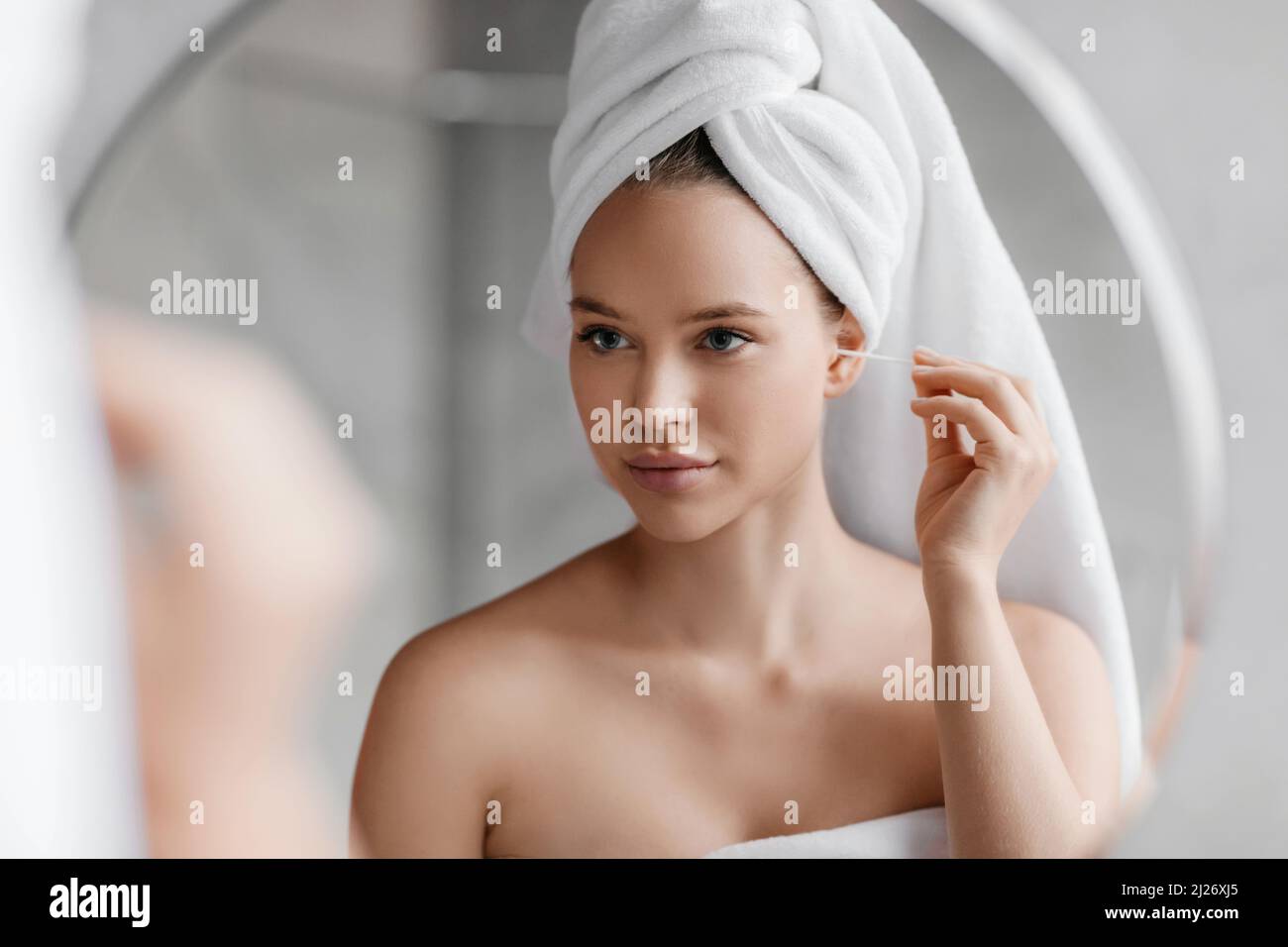 Routine igienica quotidiana. Giovane donna che pulisce le orecchie utilizzando un bastoncino di cotone mentre fa la routine di bellezza del mattino in bagno Foto Stock