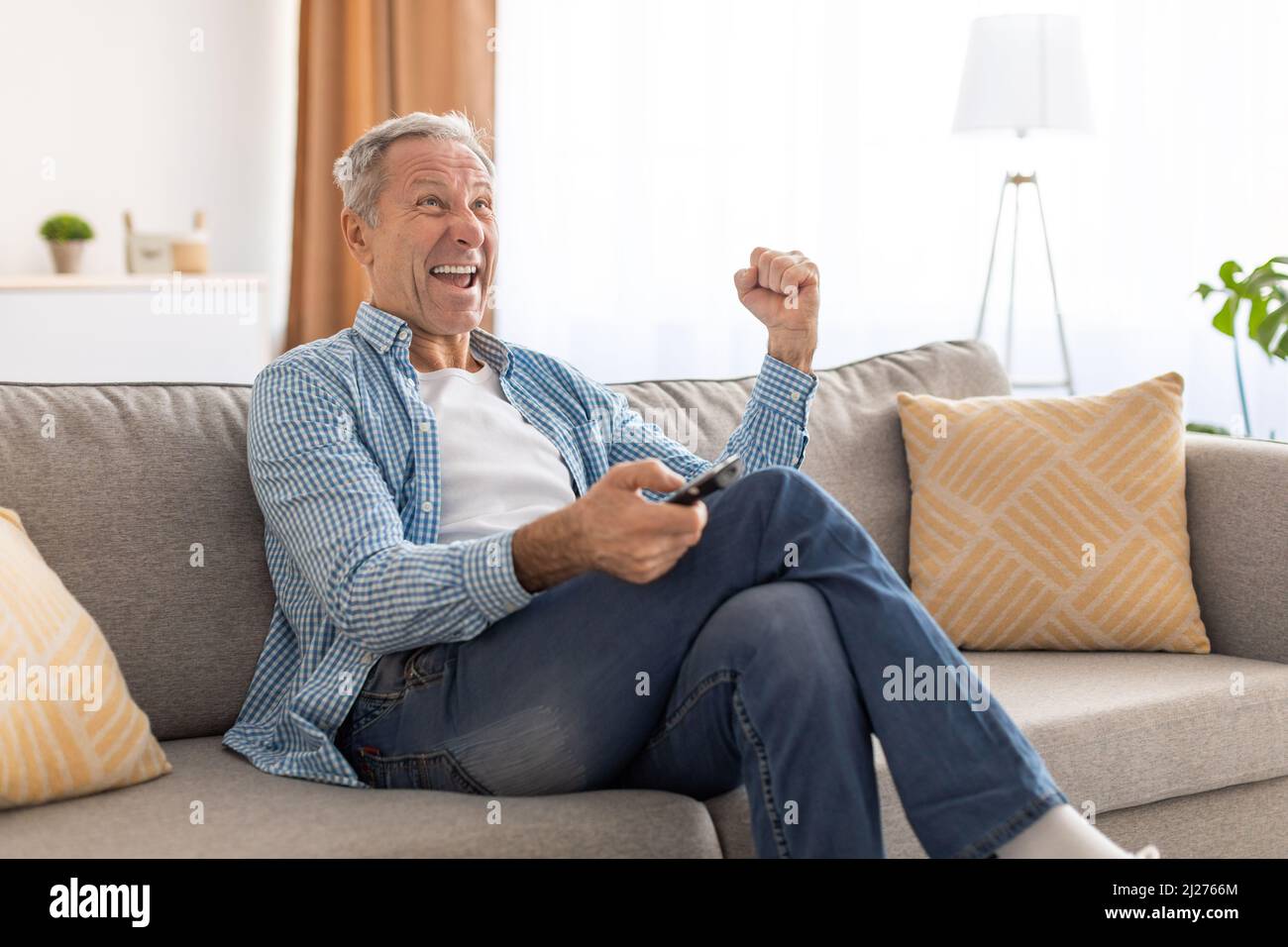 Uomo anziano eccitato che guarda la tv celebrando l'obiettivo di tenere il telecomando Foto Stock