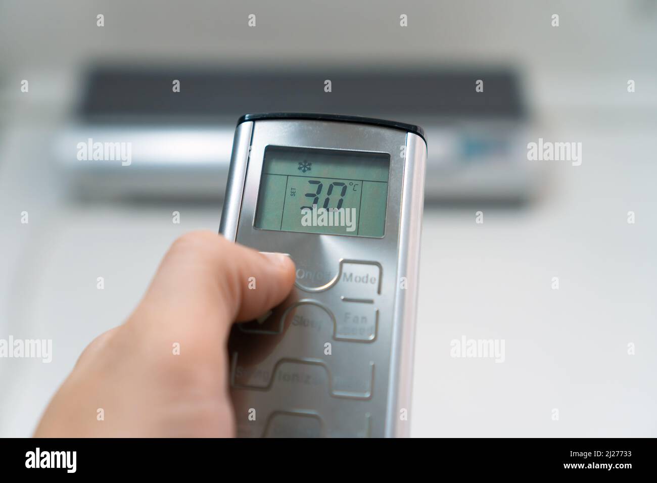 Primo piano della mano di un uomo con un telecomando grigio rivolto verso il condizionatore d'aria. Controllo della temperatura ambiente mediante un condizionatore d'aria Foto Stock