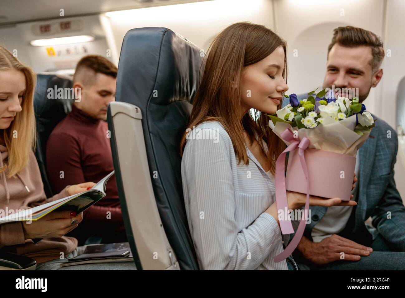 Giovane donna che odora fiori in aereo passeggeri Foto Stock